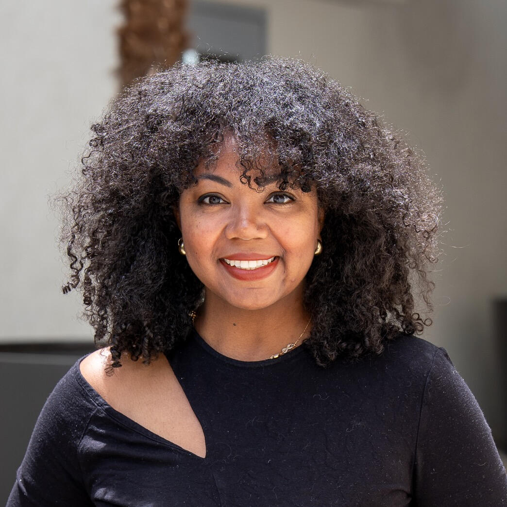 Photo of Kirstin I. Conti Picture of a smiling black woman with curly hair in a black shirt.